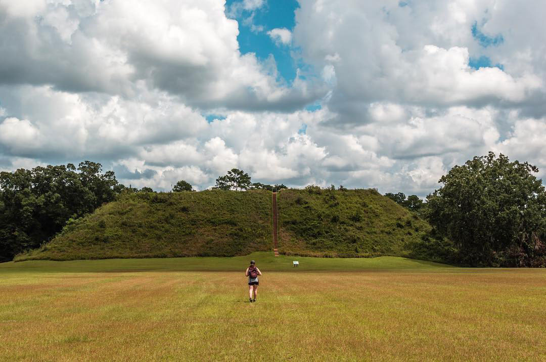 woman hiking toward a grass-covered mound