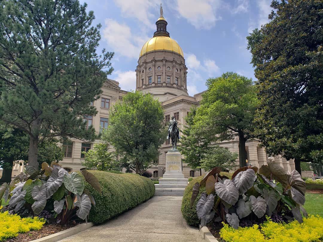 A statue of a man on horseback stands in front of the Georgia State Capitol, a large building with a gold dome. Atlanta, Georgia.
