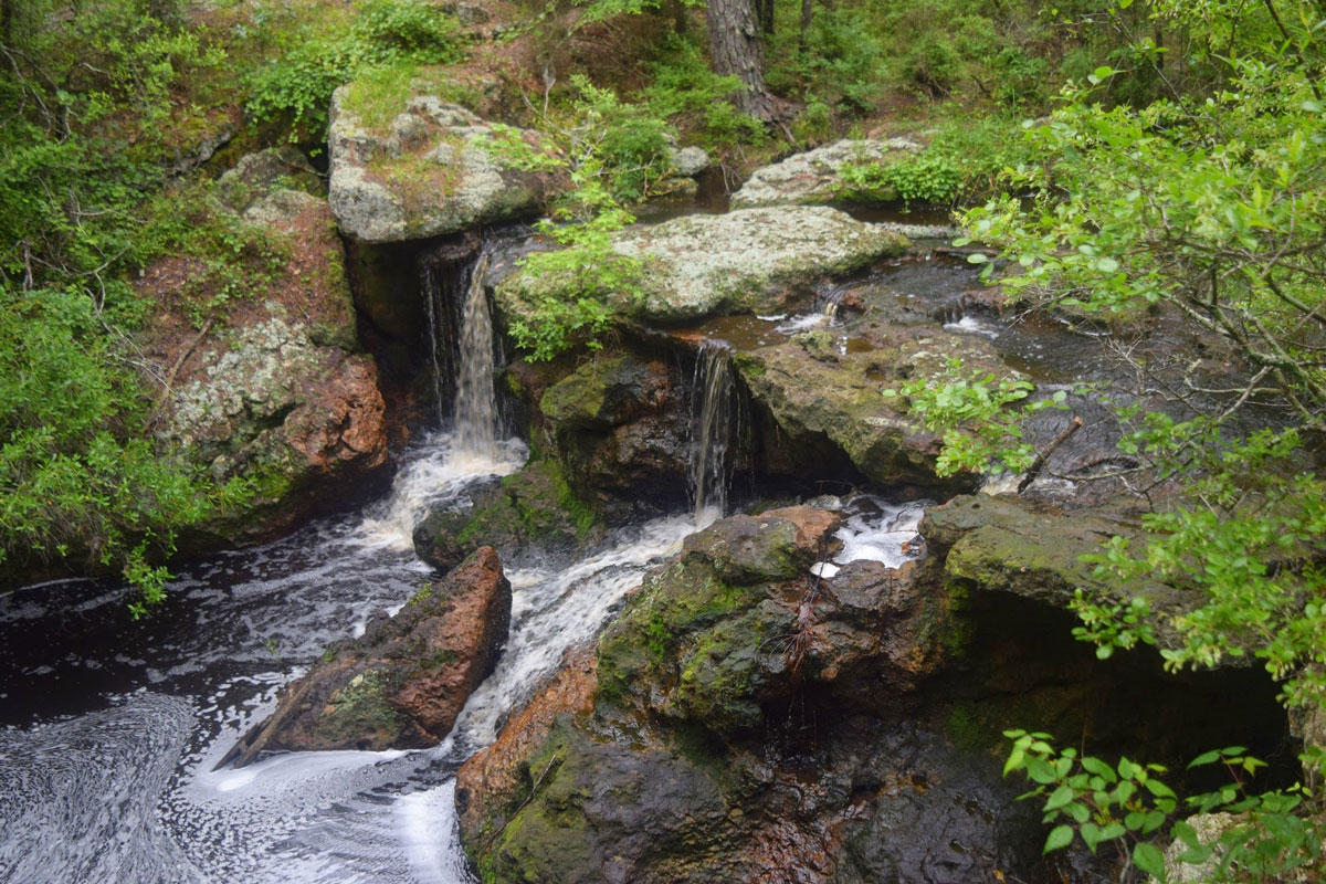 Aerial view of the rushing waterfall surrounded with greenery and large rocks at Broxton Rocks in Georgia.
