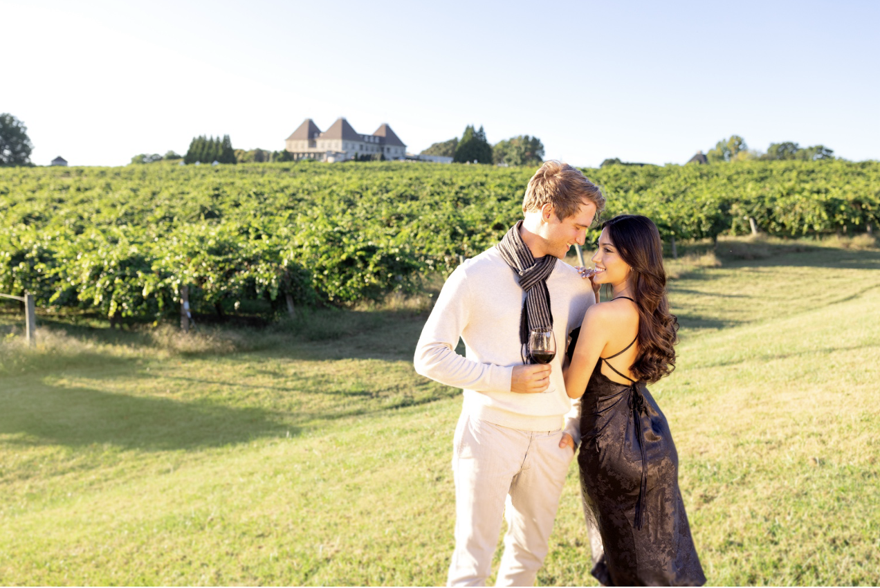 A couple embracing each other next to a vineyard and holding a wine glass at Chateau Elan Winery & Resort.