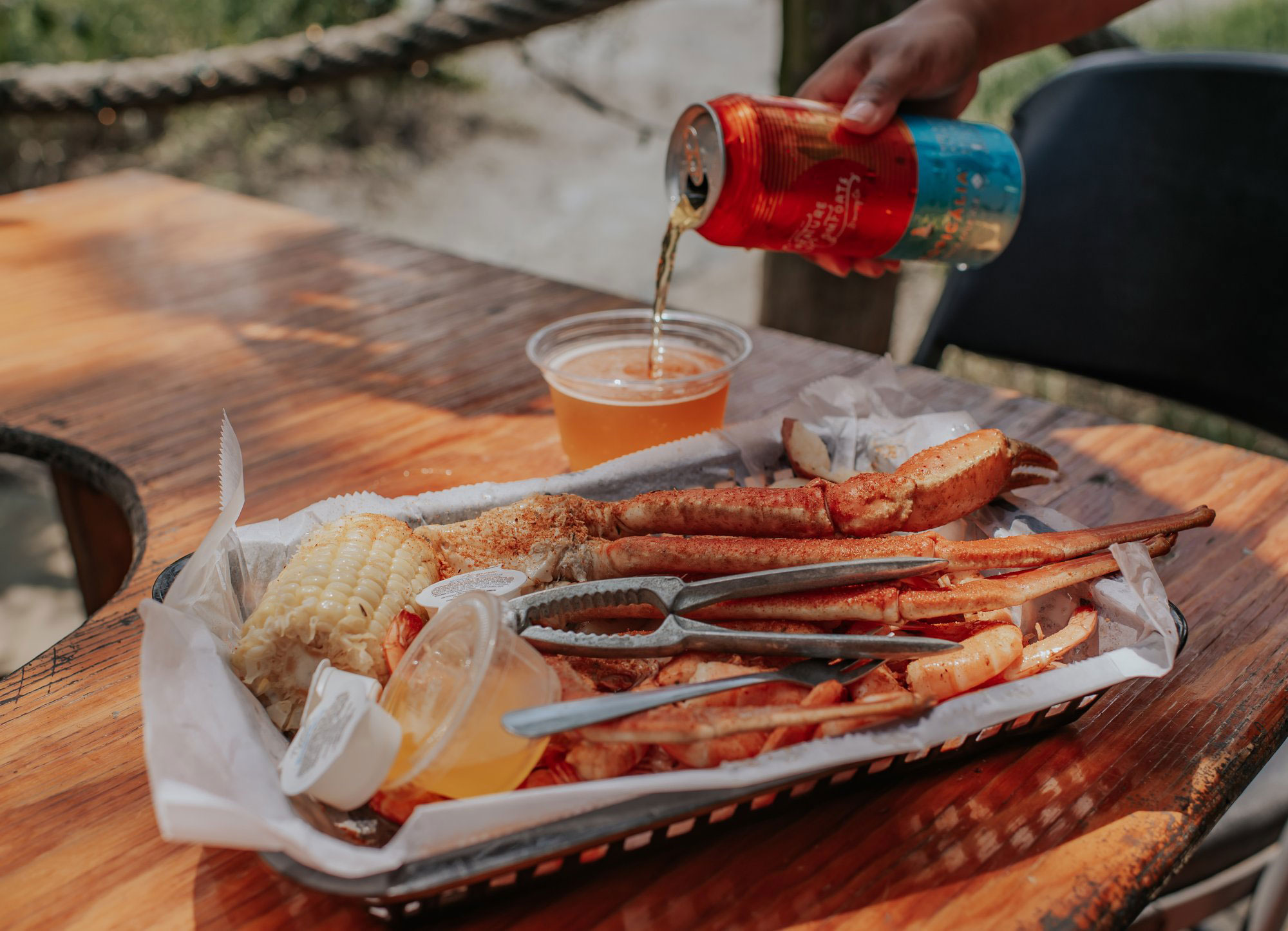 hand pouring a beer next to a basket of crab legs