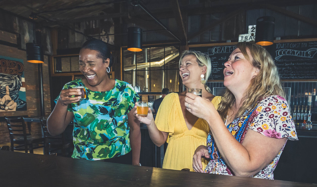 three women laughing while holding drinks at Crooked Finger Brewing in Dublin, Georgia