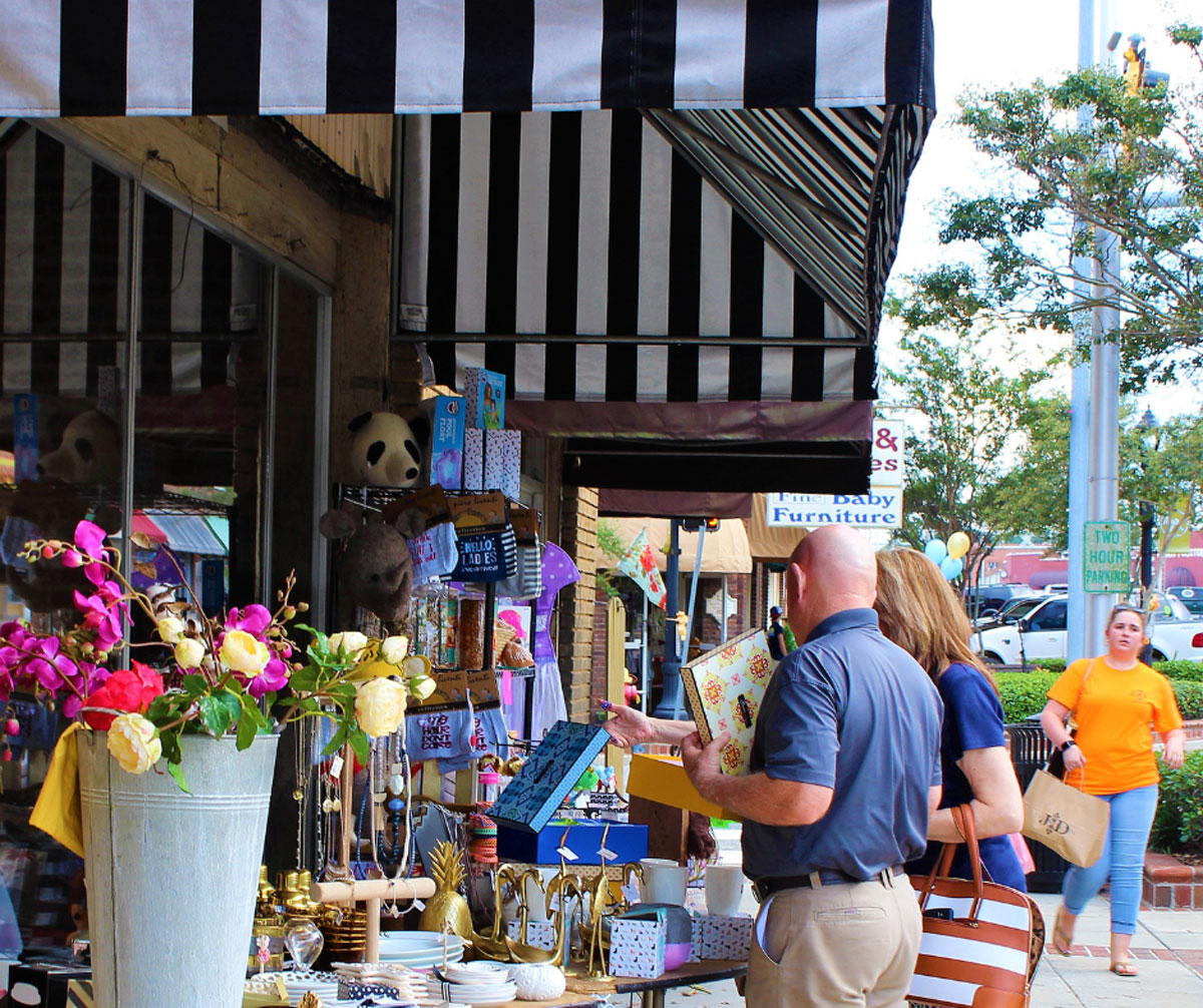 People shopping outside of shops in downtown Douglas, holding various items.