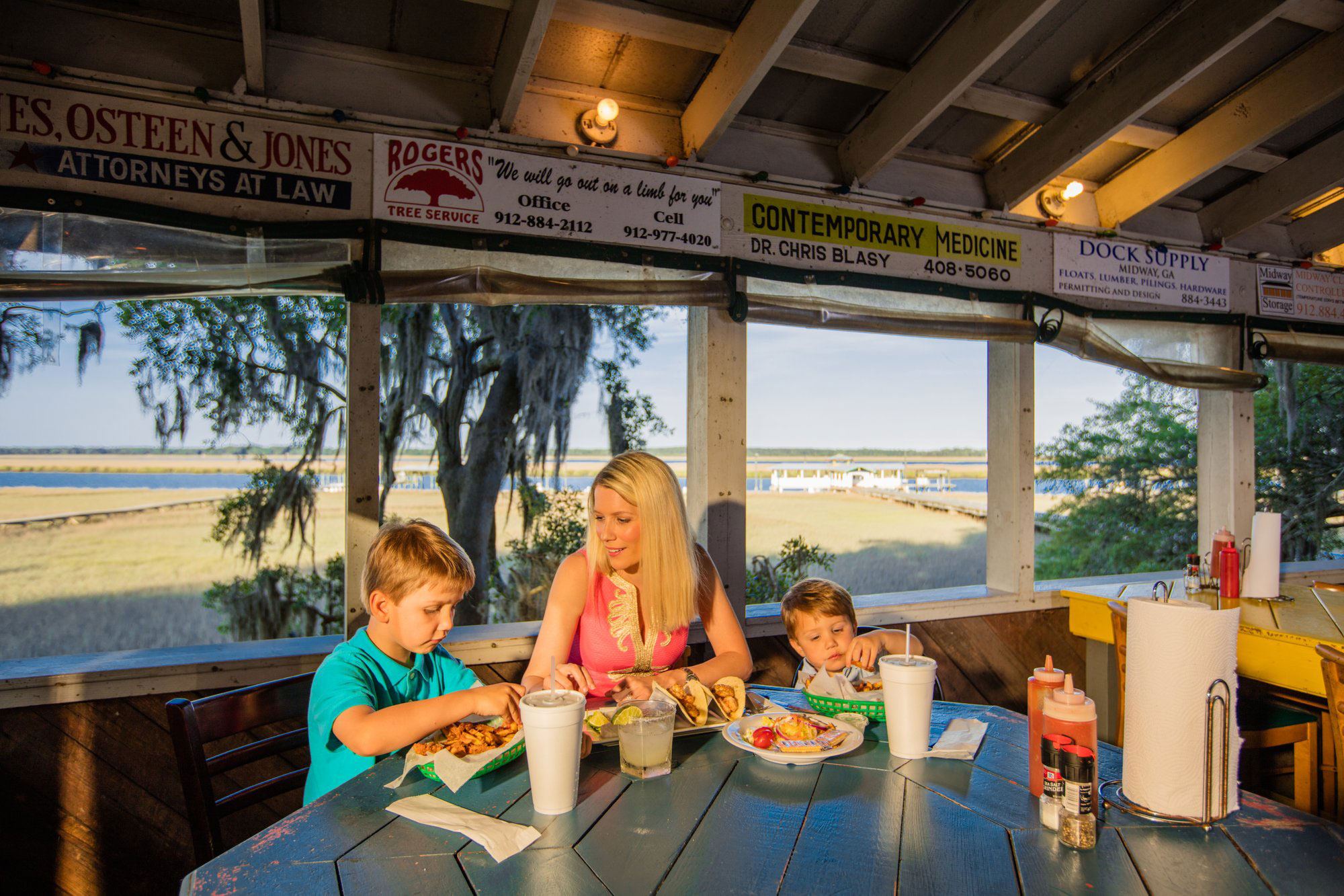 Woman and two children eating seafood with view of marsh behind them