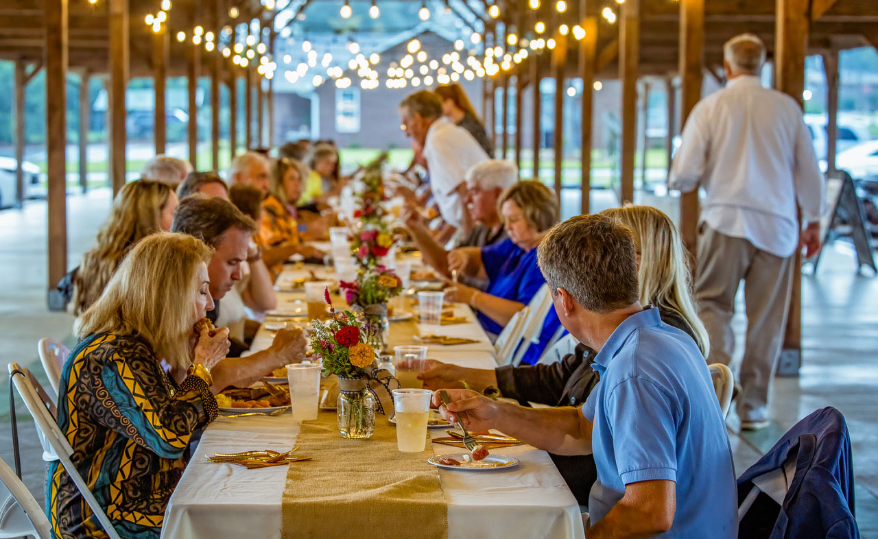 people dining at a long table under an outdoor pavilion for the Dublin Farm to Table Dinner Party
