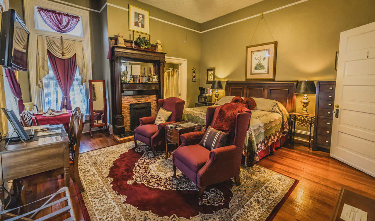 a plush guest room at the Page House B&B with two red wingback chairs, fireplace, dining table, desk, wood floors and ornate rug
