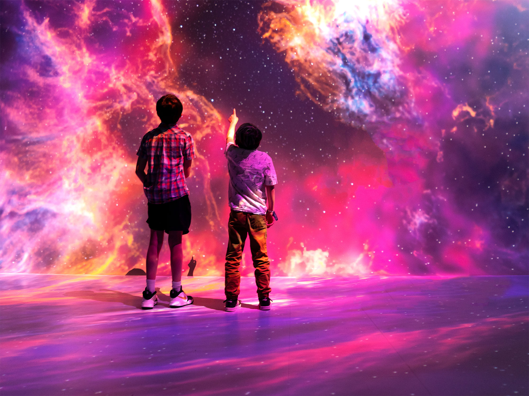 two children gaze in wonder at a pink and purple immersive image of space