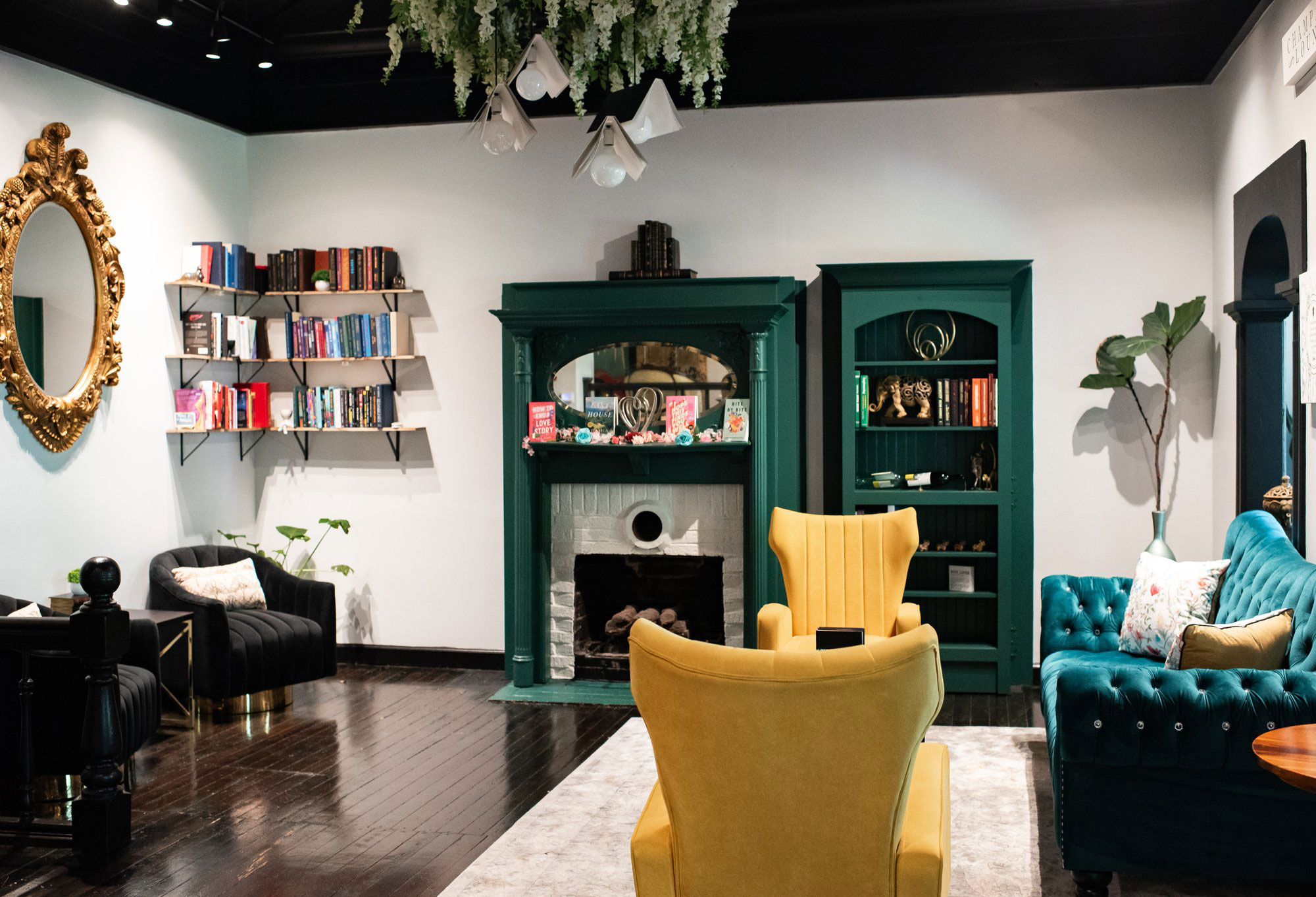 Cozy room with shelves of books, ornate oval mirror, fireplace, yellow wingback chairs and green velvet sofa at The Book Cellar