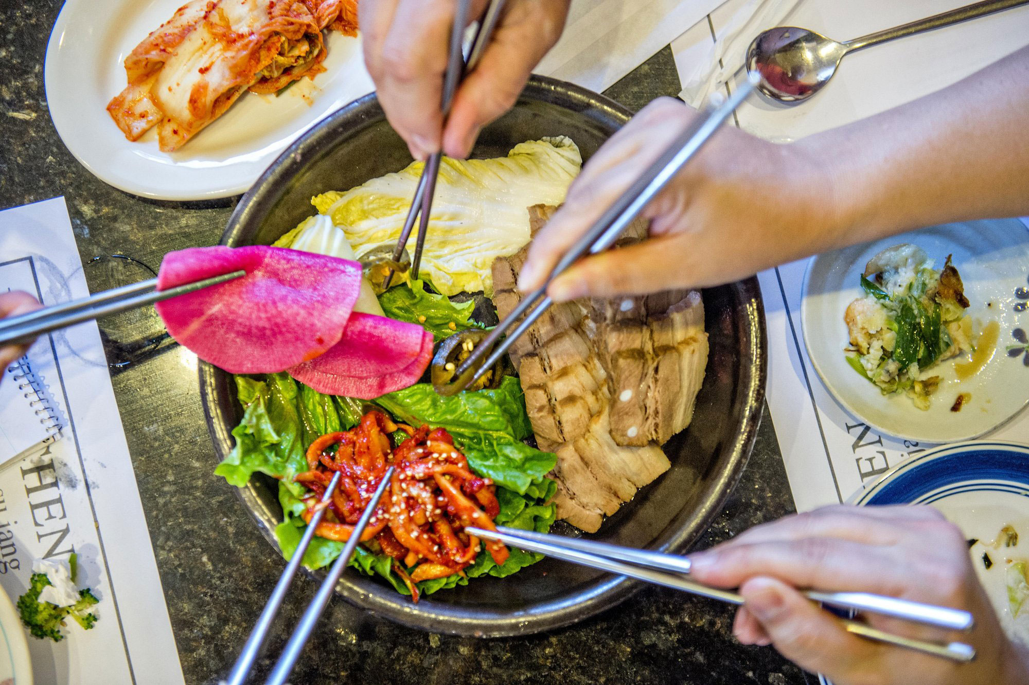 Hands using chopsticks to pick up colorful food at Jang Su Jang in Duluth, Georgia