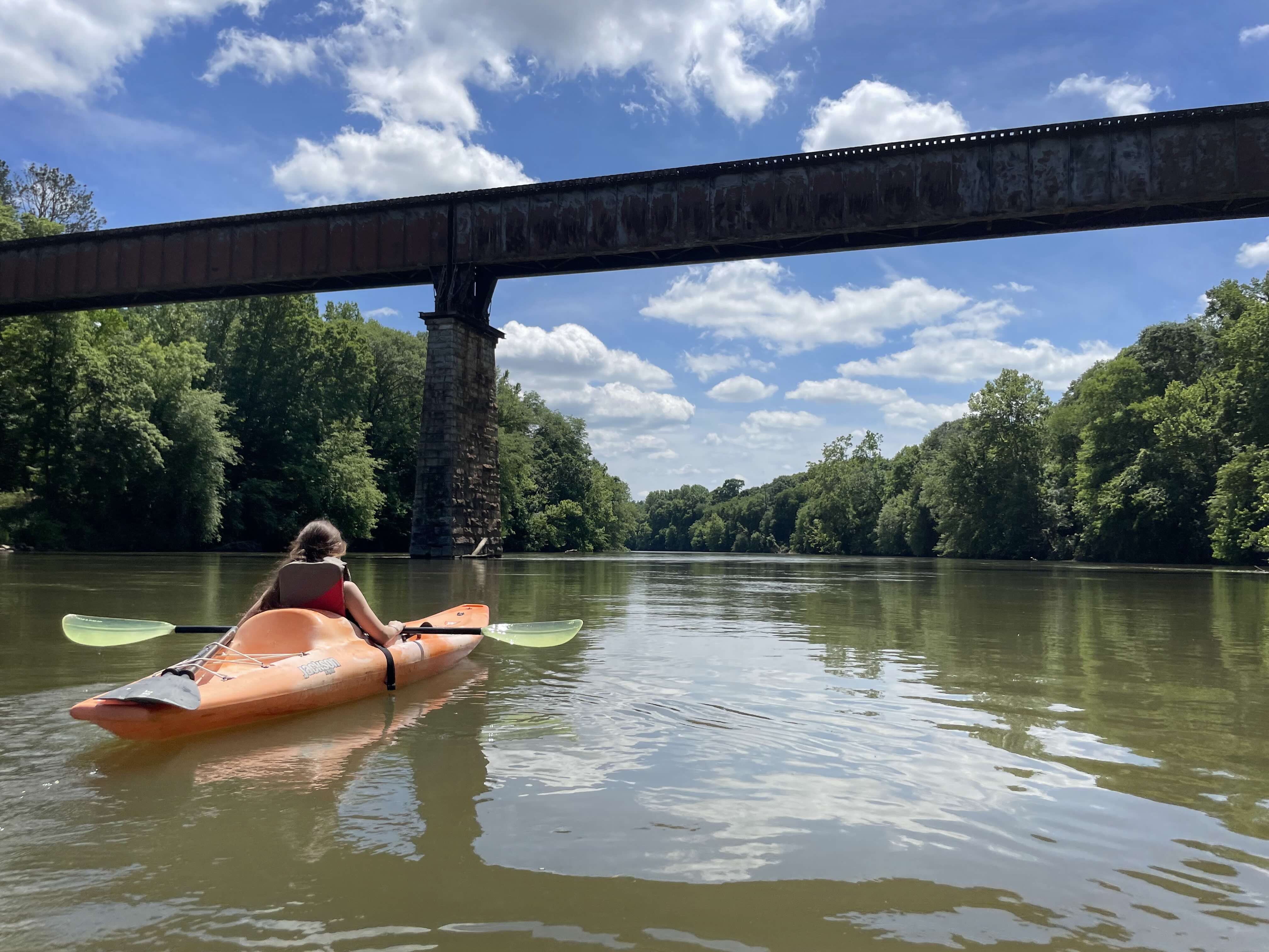 A girl in an orange kayak going under a bridge