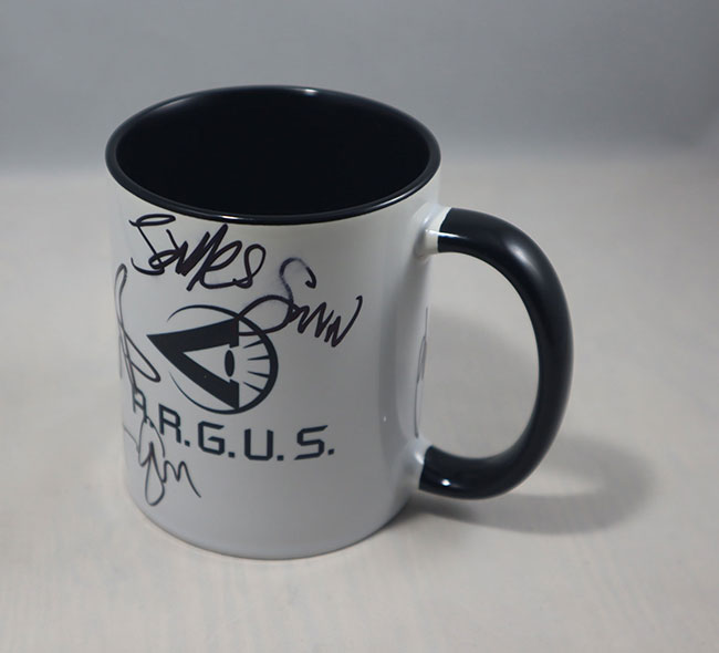 White mug with black handle and black interior with a black graphic and A.R.G.U.S. plus autographs by James Gunn, John Cena, and other cast members