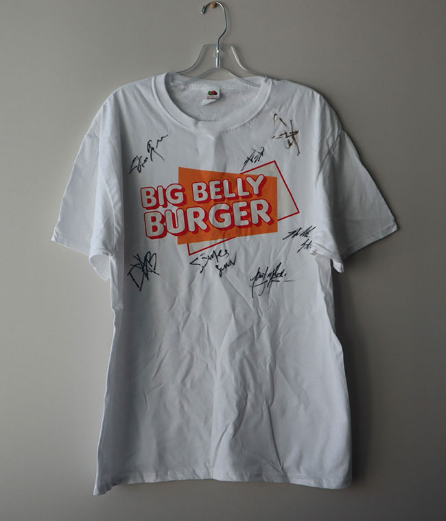 White t-shirt with an orange rectangle and the words "Big Belly Burger" plus autographs by James Gunn, John Cena, and other cast members