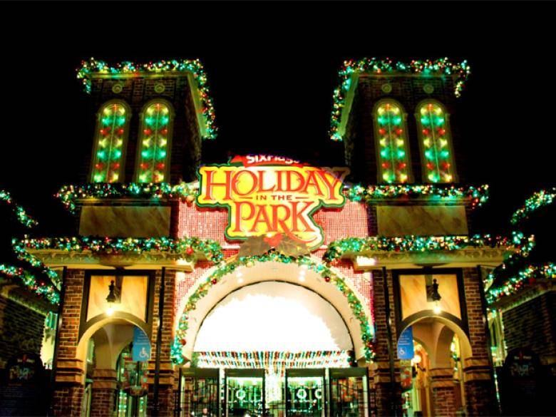A brick building at Six Flags Over Georgia in Austell is decorated with red-and-green lights. The sign at the front of the building says "Six Flags Holiday in the Park." The sky is dark behind the building.