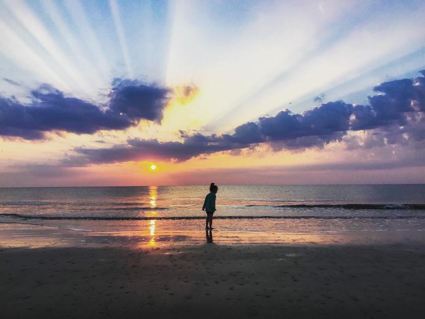 A child runs on the beach while the sun sets over the ocean behind them on a Jekyll Island, Georgia, beach.