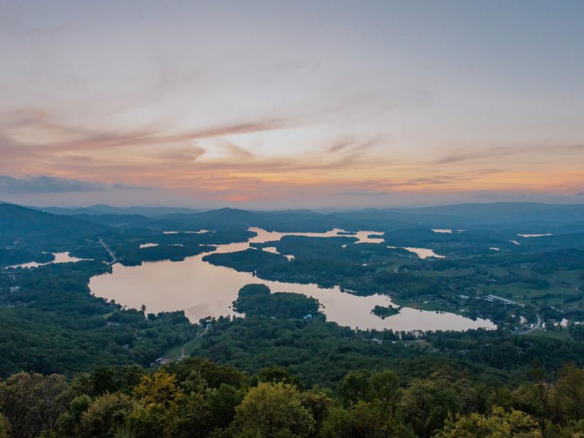 Aerial view of a large lake surrounded by trees with a sunset in the background