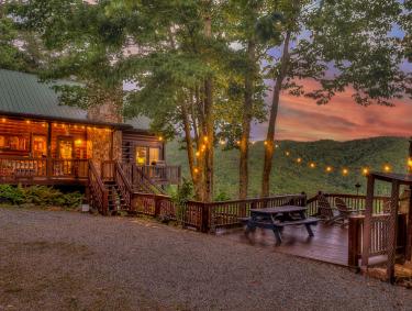 A warmly lit cabin surrounded by trees in the woods.