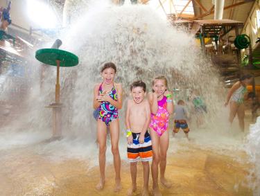 Three young children laugh on splashpad
