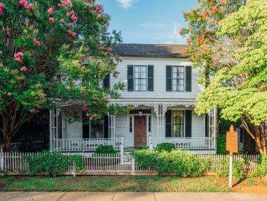 Exterior view of the Roger House Museum in Madison, Georgia, framed by bright and leafy trees.