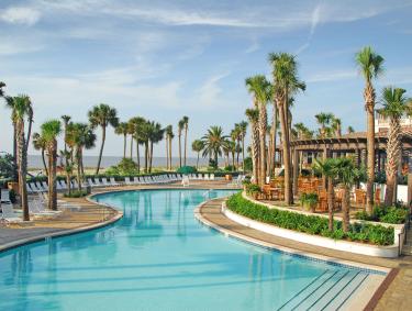 A pool winds through an outdoor resort area surrounded by palm trees.