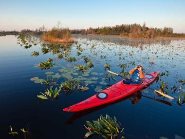 Person sits in kayak on water looking through binoculars 