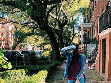woman smiles an poses outside on a residential street with trees in the background