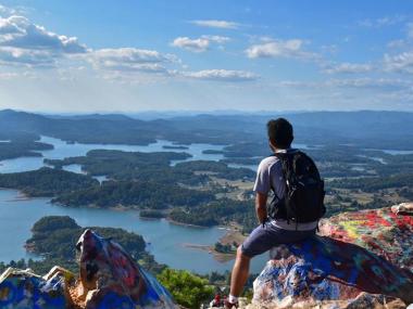 man sits on top of graffiti covered rocks overlooking rivers and trees 