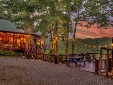 A warmly lit cabin surrounded by trees in the woods.