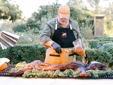 A man stands over the grill at a pig roast