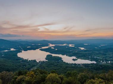 Aerial view of a large lake surrounded by trees with a sunset in the background