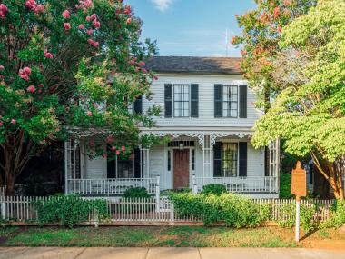 Exterior view of the Roger House Museum in Madison, Georgia, framed by bright and leafy trees.