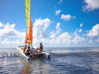 Family wearing life jackets and boating on a sunny day in the water with clouds above them.