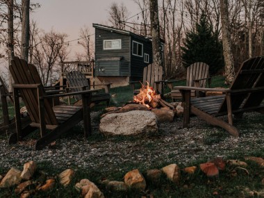 seven wooden Adirondack chairs around a fire pit with a tiny house rental in Rising Fawn, Georgia, in the background