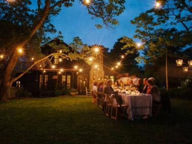 Large group of people dining outside at night under a tree lit with festive lights