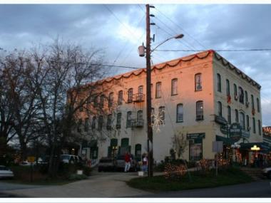 A black antique automobile sits on an exhibit for FDR in the Little White House Museum in Warm Springs, Georgia. In the background are photographs and an 1800s-looking carriage.