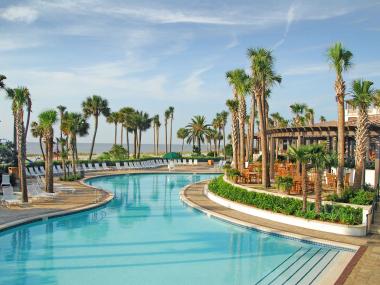 A pool winds through an outdoor resort area surrounded by palm trees.