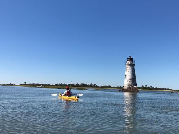 man kayaks on open water near a lighthouse