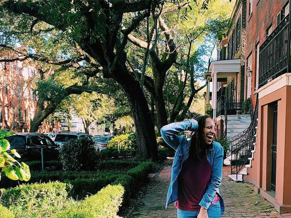 woman smiles an poses outside on a residential street with trees in the background