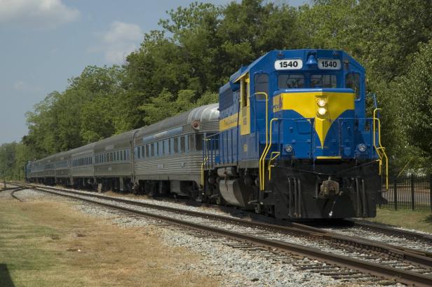 A train runs along the tracks with trees in the background.