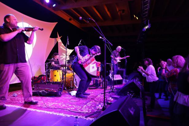 Live-music artist, Steve Riley, performs with their band on a purple-lit stage at Savannah Music Festival in Georgia.