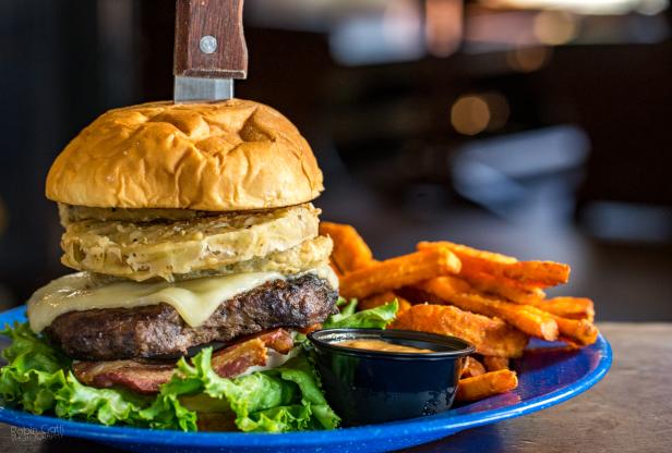 big burger with fried green tomato and a knife through the top with a side of sweet potato fries