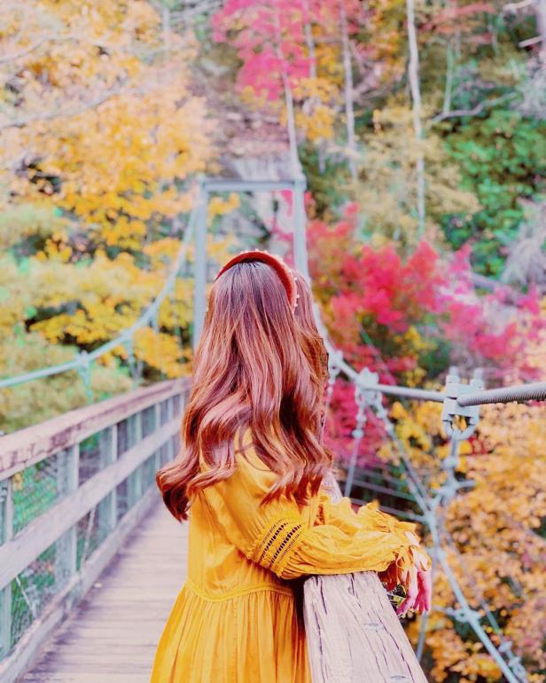A girl walks across a swinging bridge surrounded by fall foliage