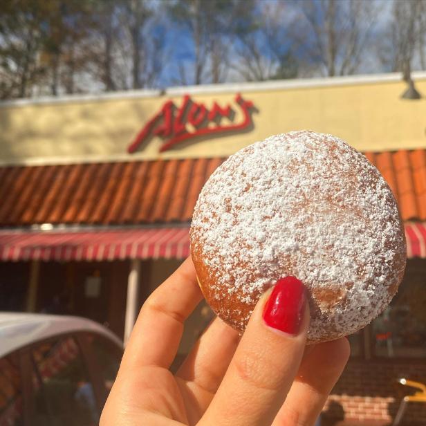 Woman's hand holding a powder sugar-coated cookie in front of Alon's Bakery in Virginia Highlands