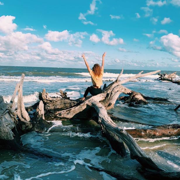 Woman sitting on a tree on Driftwood Beach on Jekyll Island, Georgia. Photo by @mollymartin_44