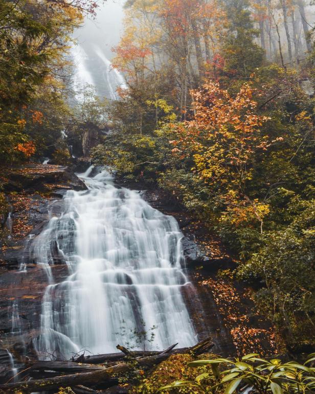 A large waterfall is surrounded by colorful fall foliage.