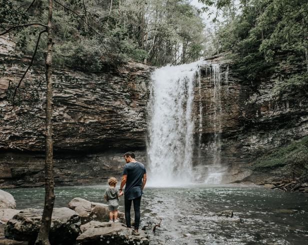 Father and son standing on a rock holding hands near a waterfall at Cloudland Canyon State Park in Georgia. Photo by @gcalebjones