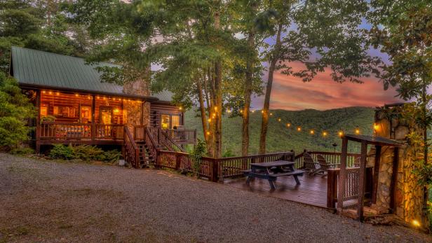 A warmly lit cabin surrounded by trees in the woods.