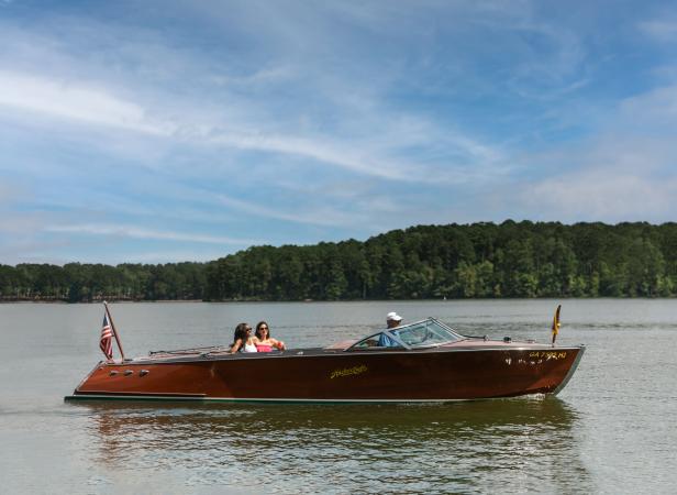 Three people on a brown Hacker Craft boat on Lake Oconee in Greensboro, Georgia.