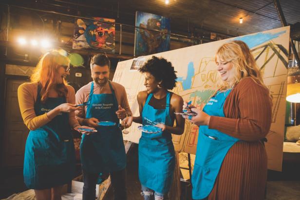 Four people wearing blue "Greater Augusta Arts Council" aprons and holding paint palettes at the Promenade & Paint experience in Augusta, Georgia