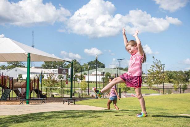 A young girl prepares to do a cartwheel under blue skies with fluffy clouds with playground equipment in the background