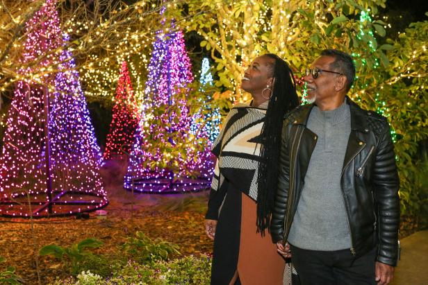 Couple holding hands walking by colorfully lit Christmas trees